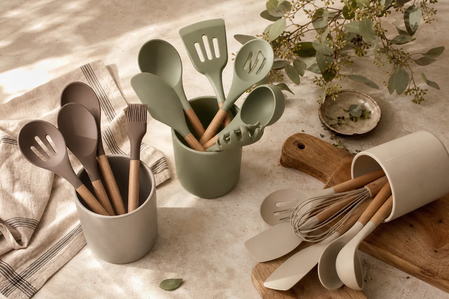 Sage, charcoal, and cream silicone utensils arranged on a warm cream kitchen counter with linen and herbs.